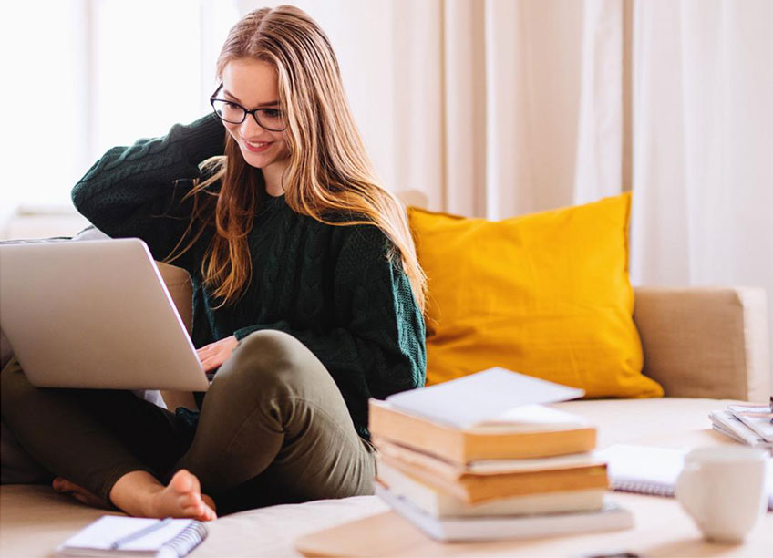 Junge Studentin sitzt mit ihrem Laptop auf dem Sofa und lernt online eine neue Sprache